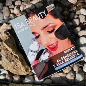 Copertina di Isa Beauty Magazine con un primo piano di una donna che sorride e applica prodotti di bellezza, in un ambiente naturale.